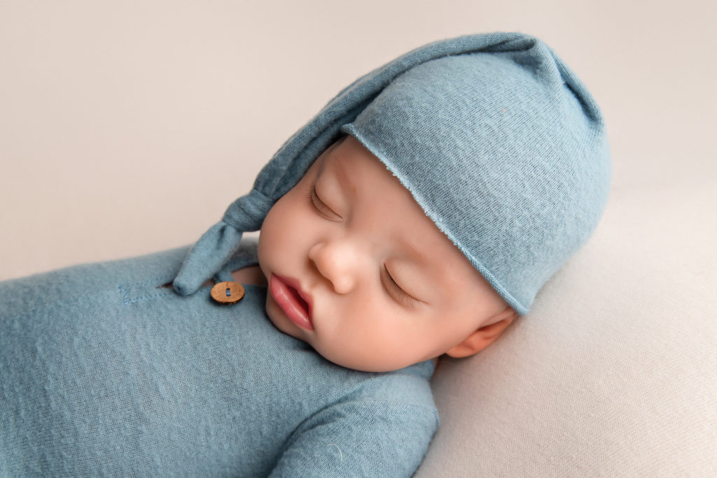 baby boy sleeps in blue newborn outfit and cap during Las Vegas Studio newborn portraits